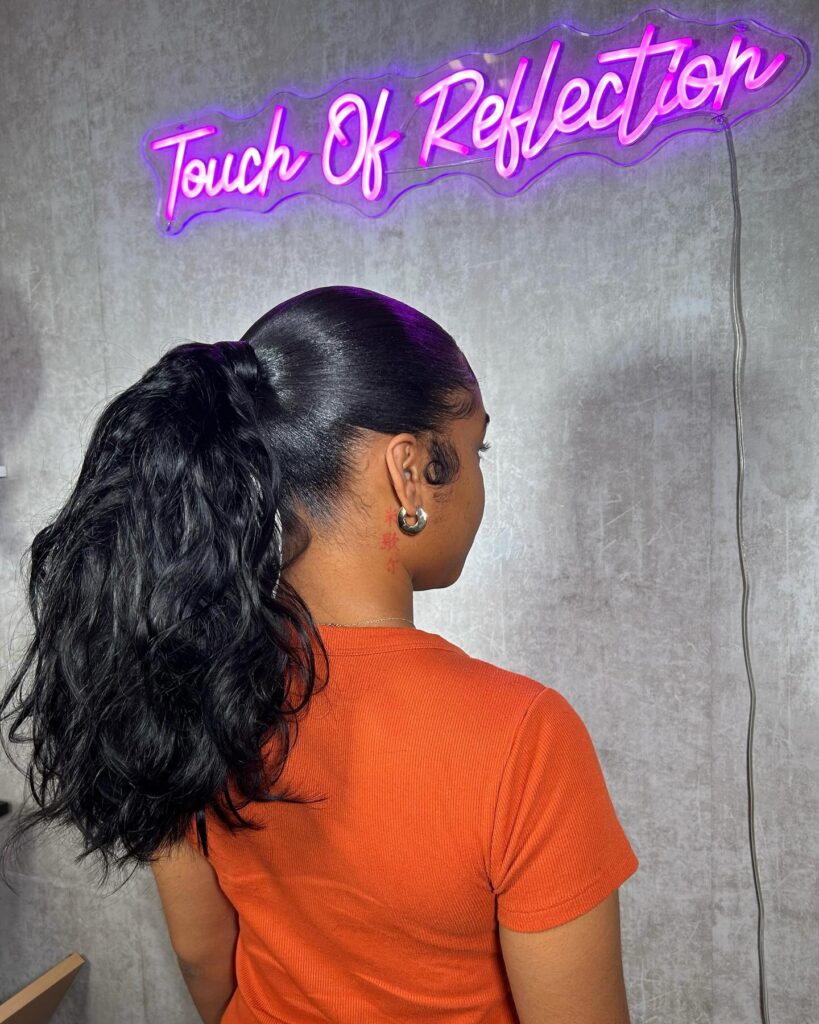 A woman from the side wearing a glossy black mid-height ponytail with voluminous beach waves and styled baby hairs.