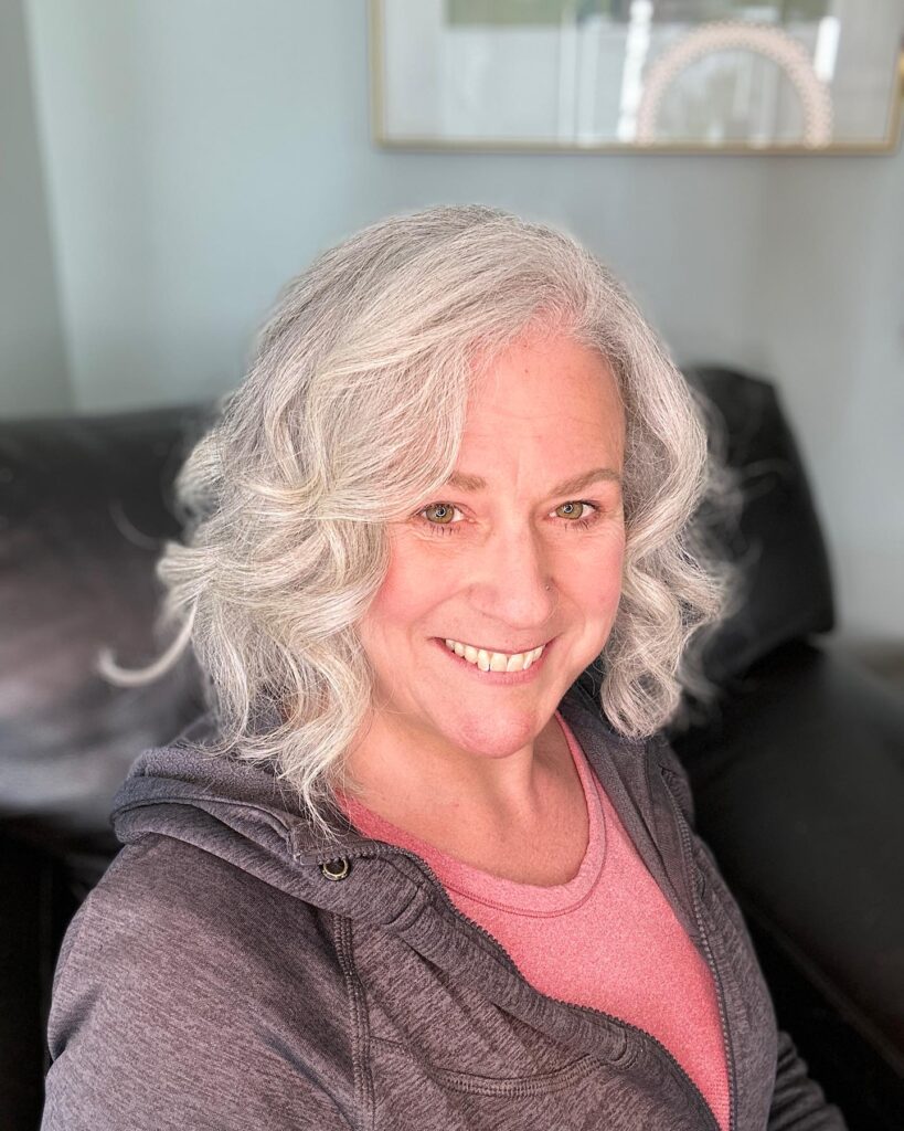 A woman with shoulder-length silver hair styled in soft, bouncy waves and face-framing layers.