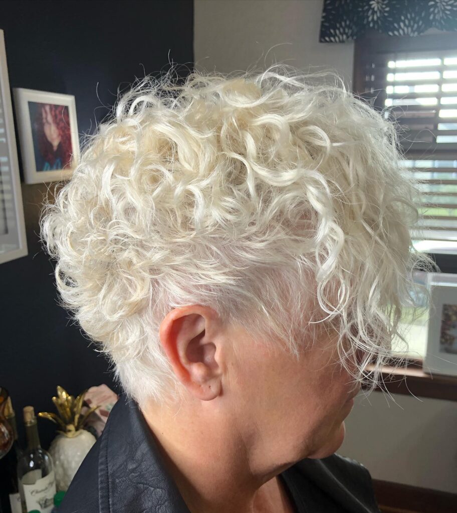 A woman seen from the side with a short, snowy white pixie cut featuring bouncy curls and a wispy fringe.