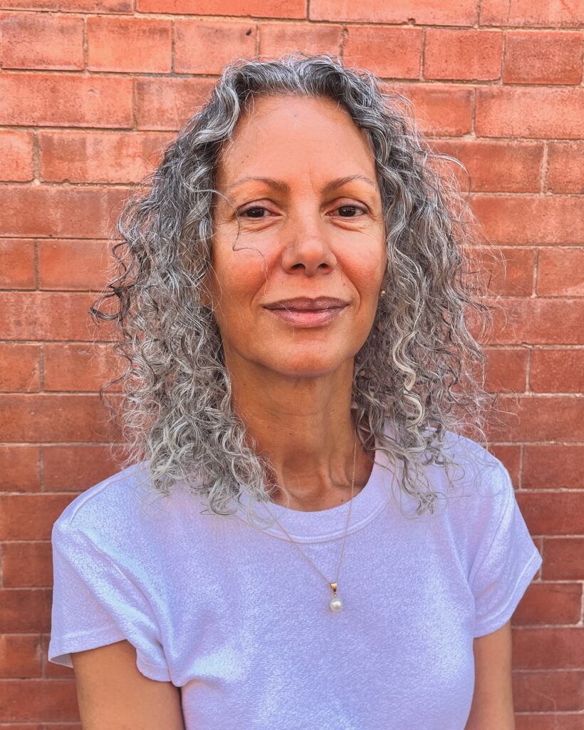A woman with mid-length salt-and-pepper curly hair falling just past the shoulders.