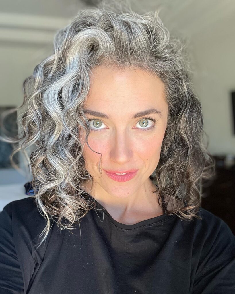 A woman with shoulder-length salt and pepper curls swept to one side for a voluminous and layered look.