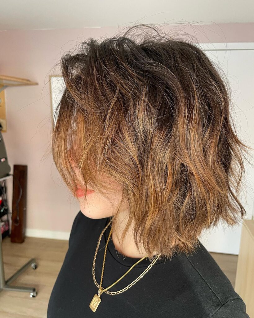 A side profile of a woman with a medium-length textured bob featuring copper highlights and messy waves.