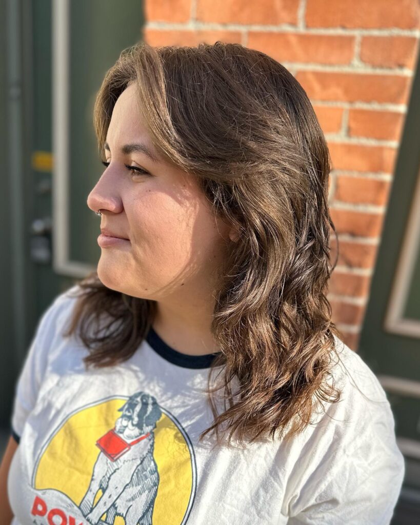A side profile of a woman with medium-length wavy brown hair and subtle caramel highlights.