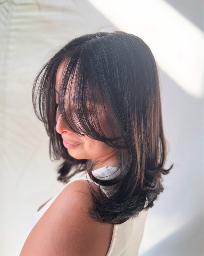 Shoulder length dark layered haircut with soft face framing pieces and inward curved ends.