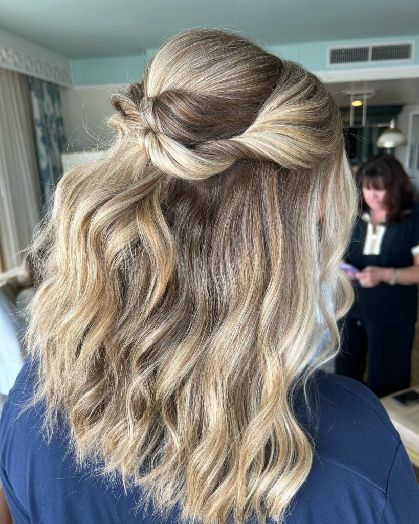 Long blonde wavy hair styled in a half up twist with loose textured waves.