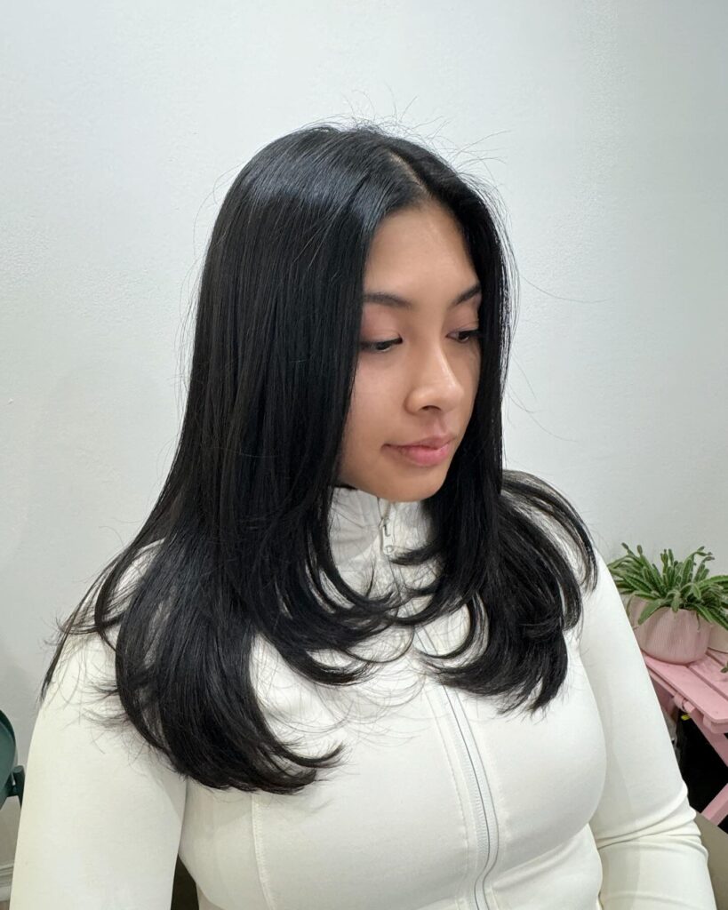A woman with glossy mid length black hair featuring internal layers that curl inward at the ends.