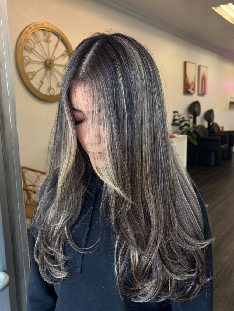 A woman with long medium length dark hair featuring heavy ash blonde highlights and soft inward curving layers.