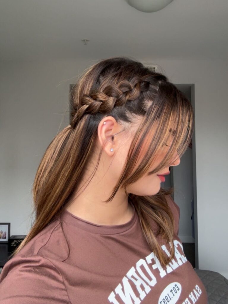 A side view of a woman with highlighted brown hair styled in a low ponytail with a thick braid along the side of her head.