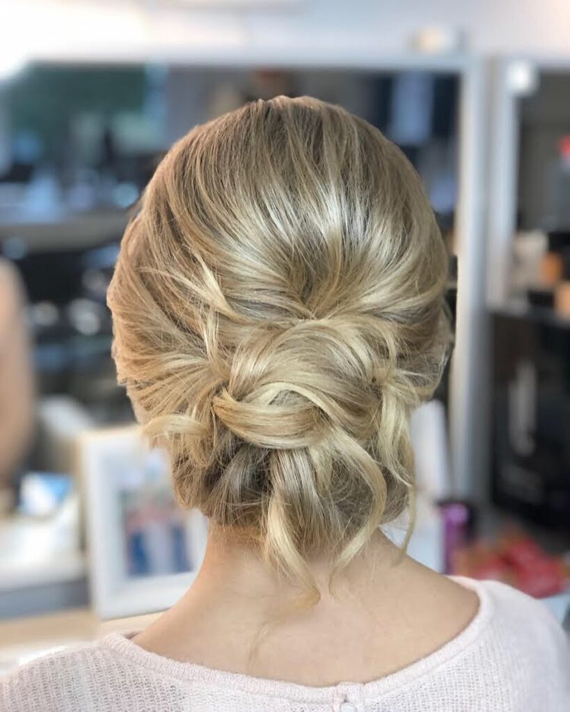 A back view of a woman with blonde hair styled into a soft and messy low chignon updo.