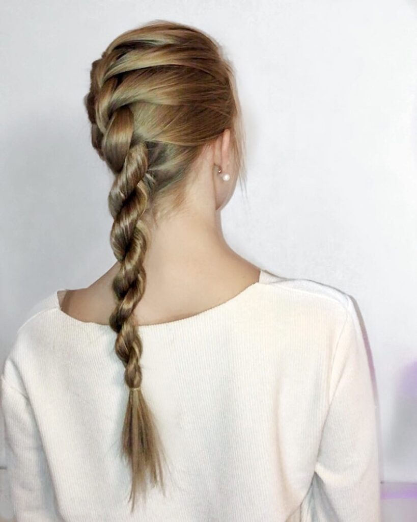A back view of a woman with long blonde hair styled in a French braid that turns into a two strand rope twist ponytail.