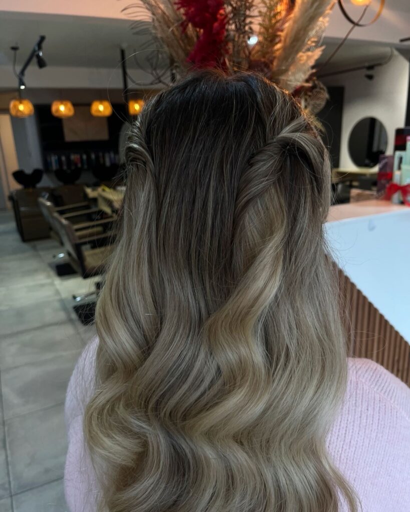 A back view of long wavy blonde hair styled in a half up look with twisted sections pinned at the crown.