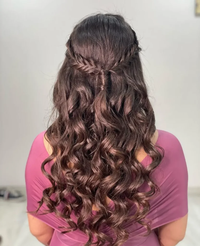 A back view of long dark curly hair featuring a half up braided crown that meets in the center.