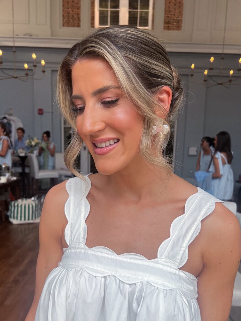 A woman with bright blonde face framing highlights wears a textured low updo with wavy strands around her face.