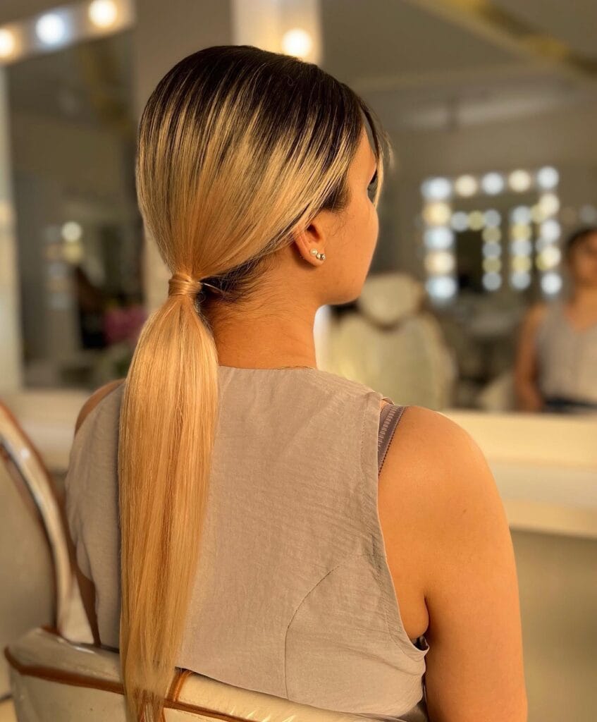 Blonde low ponytail with a smooth sleek finish and subtle dark root blend.