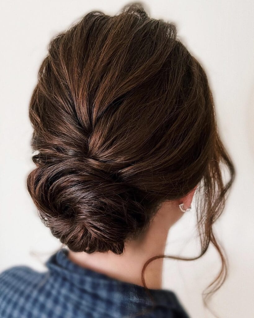 Dark brown hair styled in a textured twisted low bun with loose face framing strands.