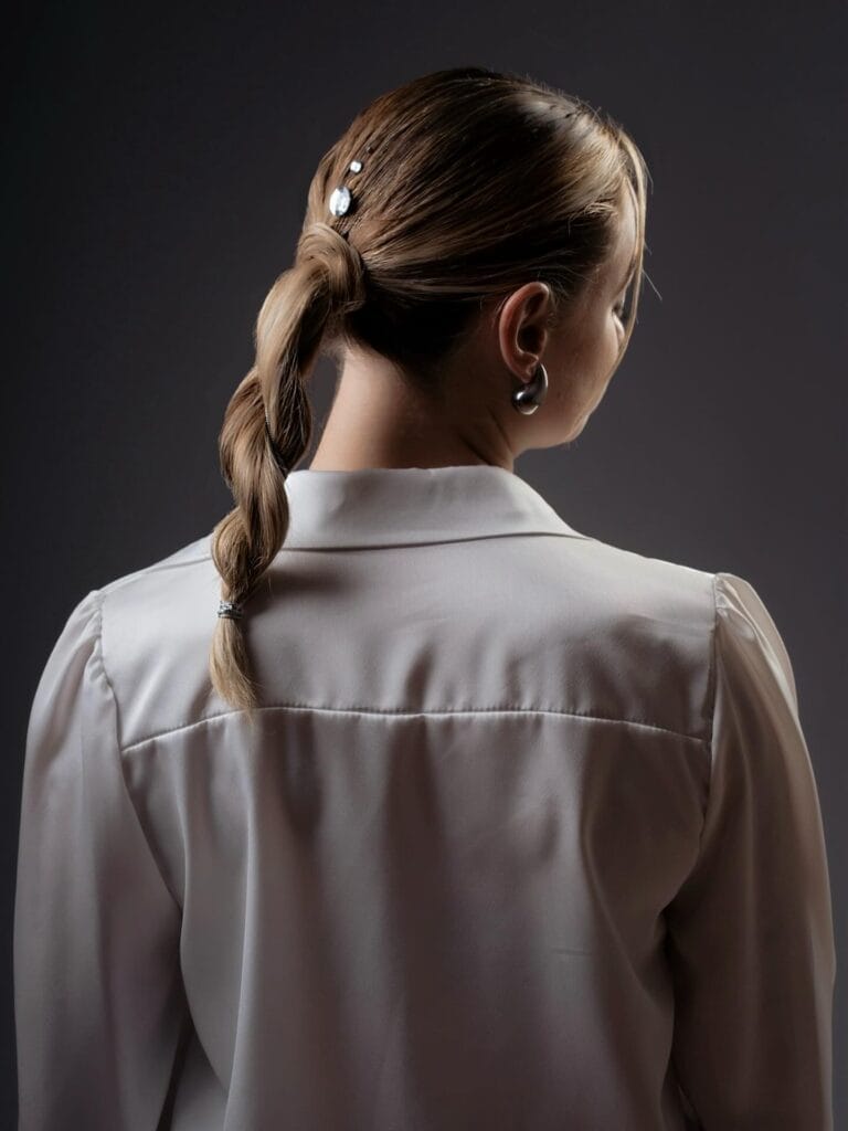 Blonde hair styled into a sleek low ponytail with a structured braid running down the back.