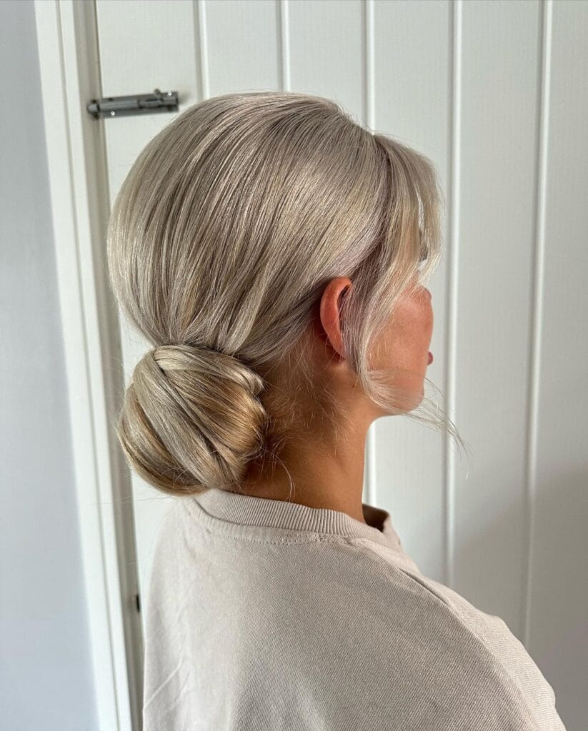 Blonde hair styled in a smooth low twisted bun with a soft side part.