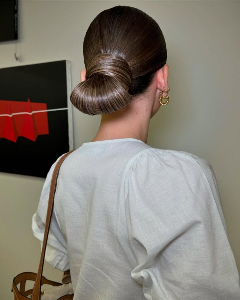 Dark brown hair styled into a glossy and sculpted low bun with a smooth finish.