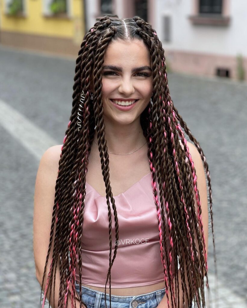 A smiling woman wearing very long dark brown rope twists featuring bright pink highlights and small silver hair jewelry.
