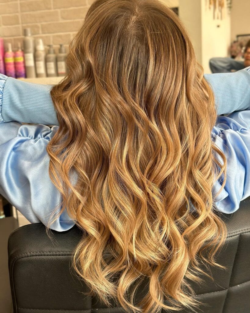 Long caramel toned hair with defined wavy texture and golden highlights.