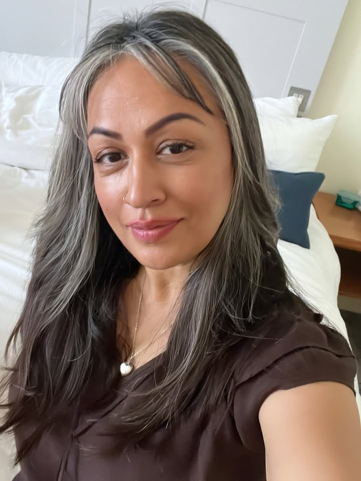 Shoulder length dark hair with silver streaks and soft natural bangs framing the face.