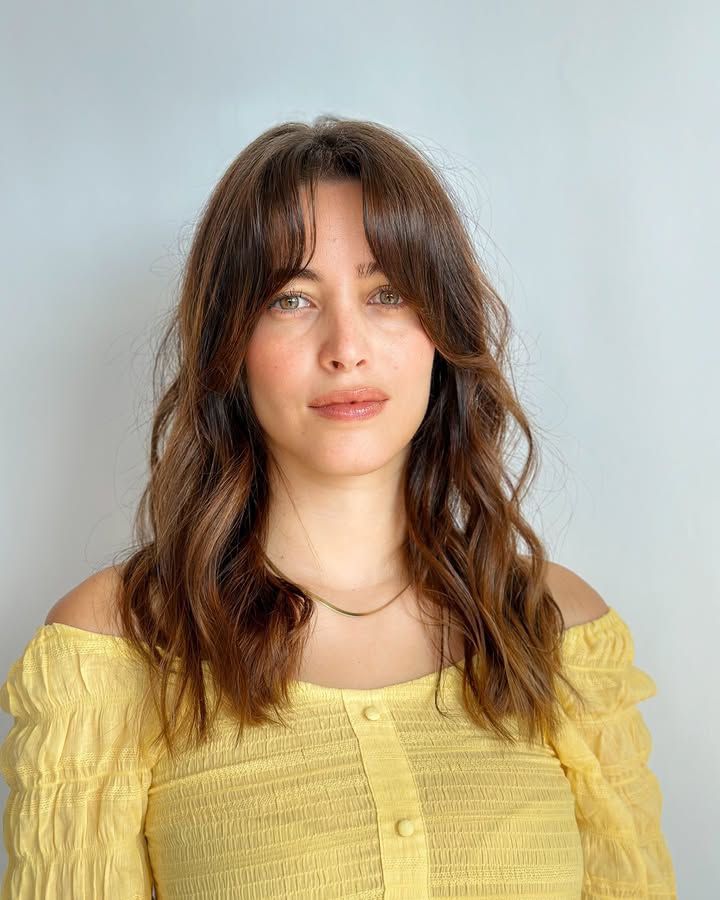 Shoulder length brunette wavy hair with wispy bangs and a soft textured finish.