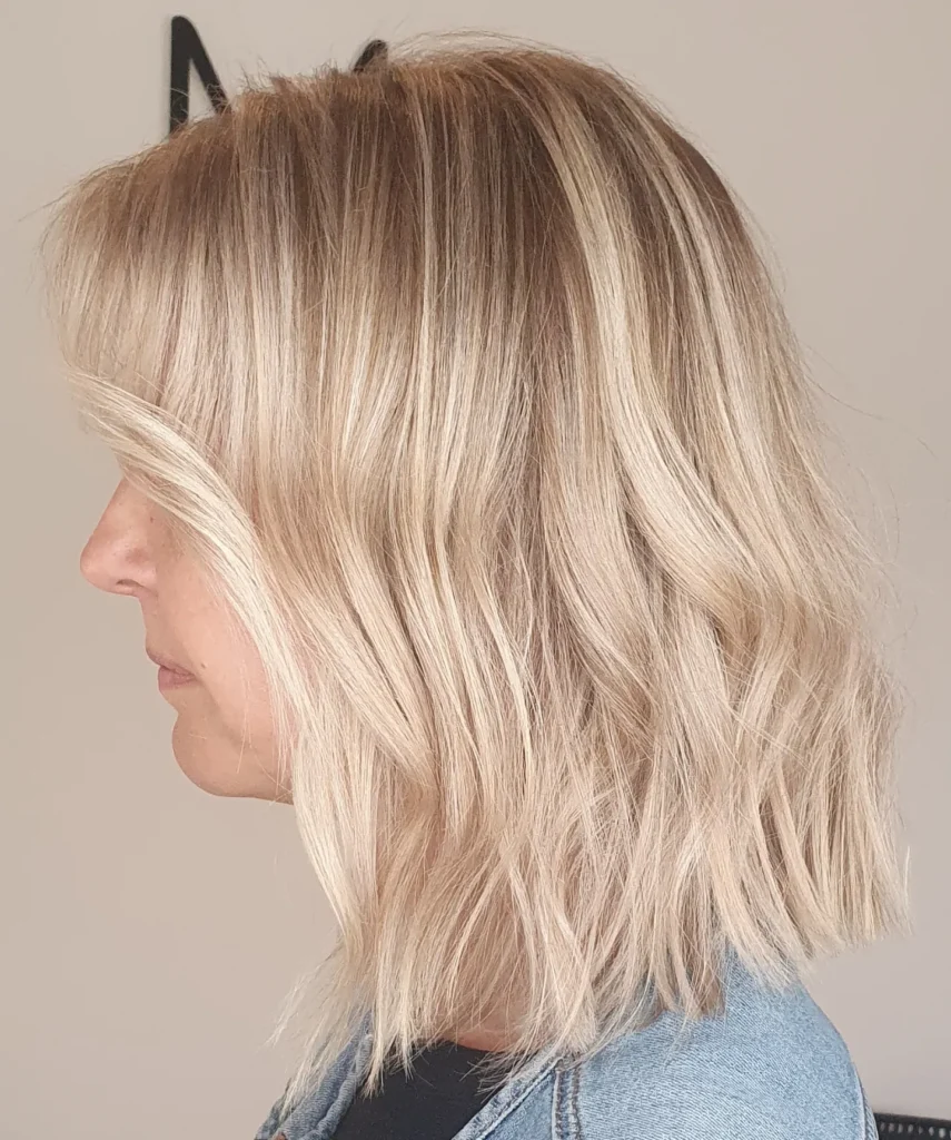 A side profile of a woman with a textured champagne blonde lob featuring subtle waves and a soft root smudge.