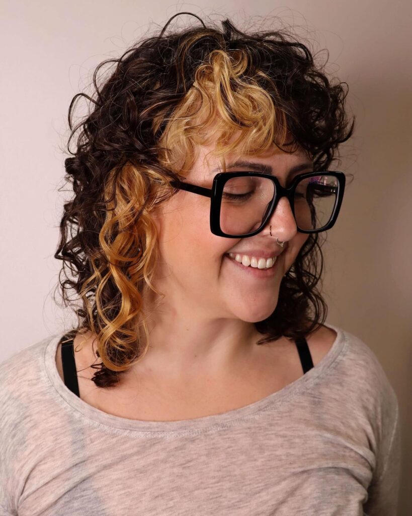 A woman with a two-tone curly shag haircut featuring dark brown hair and bold blonde face-framing highlights.