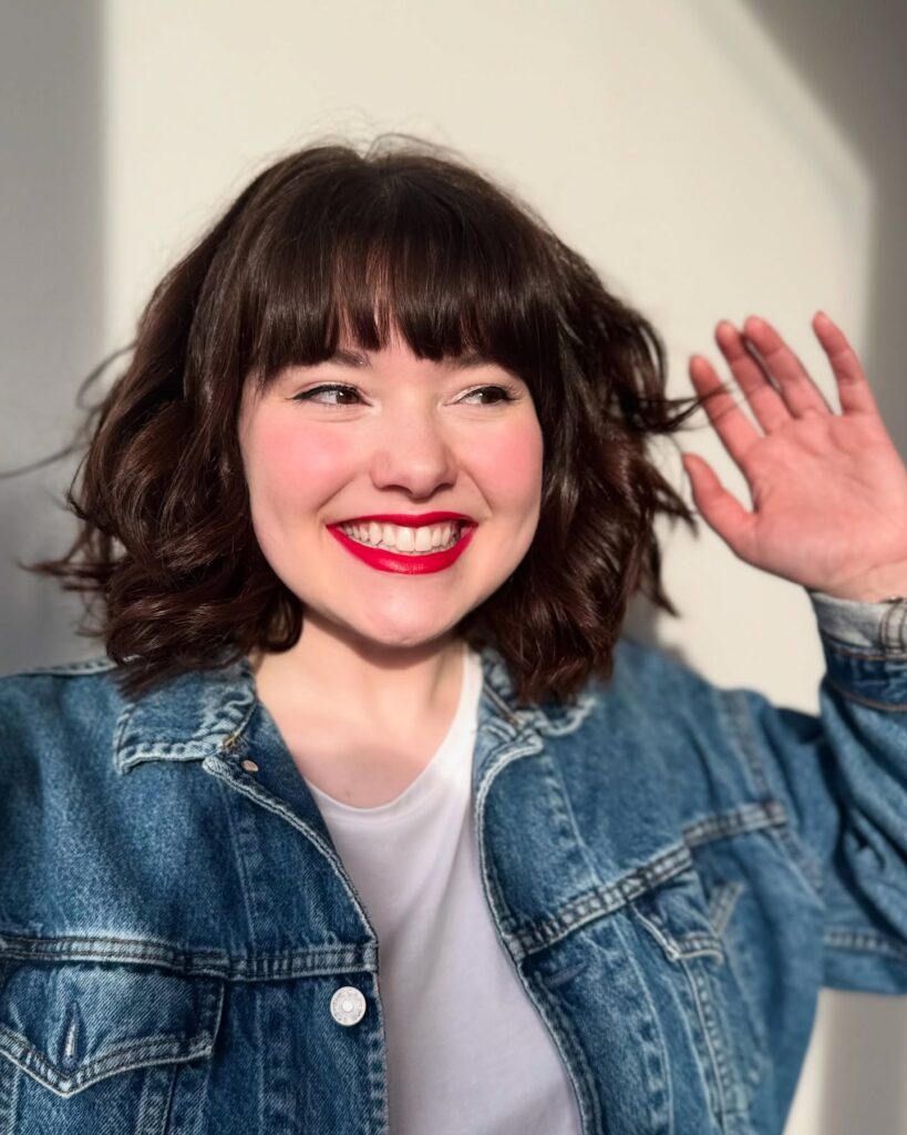 A smiling woman with a chocolate brown wavy bob and thick blunt-cut bangs.