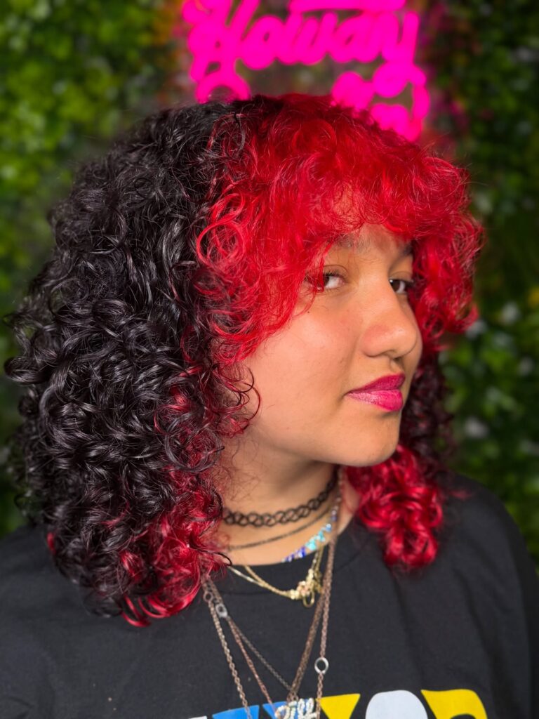 A woman with a shoulder-length curly lob featuring a bold split-dye look with black and bright red curls.