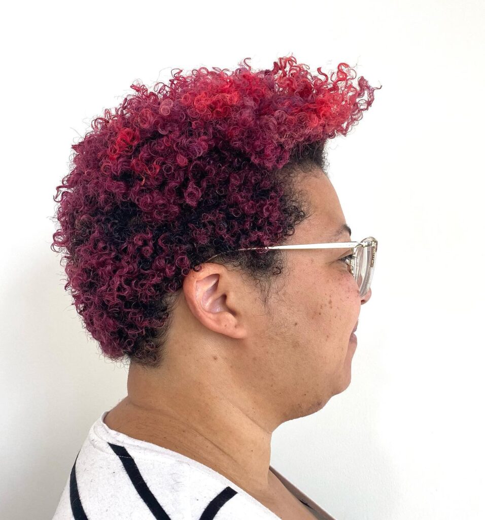 A side profile of a woman with a short, tapered afro featuring a magenta and plum purple ombre color.