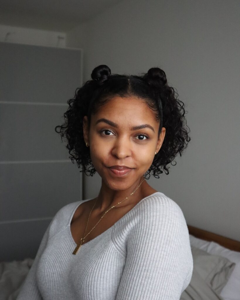 A woman with short dark curly hair styled into two small half-up space buns.