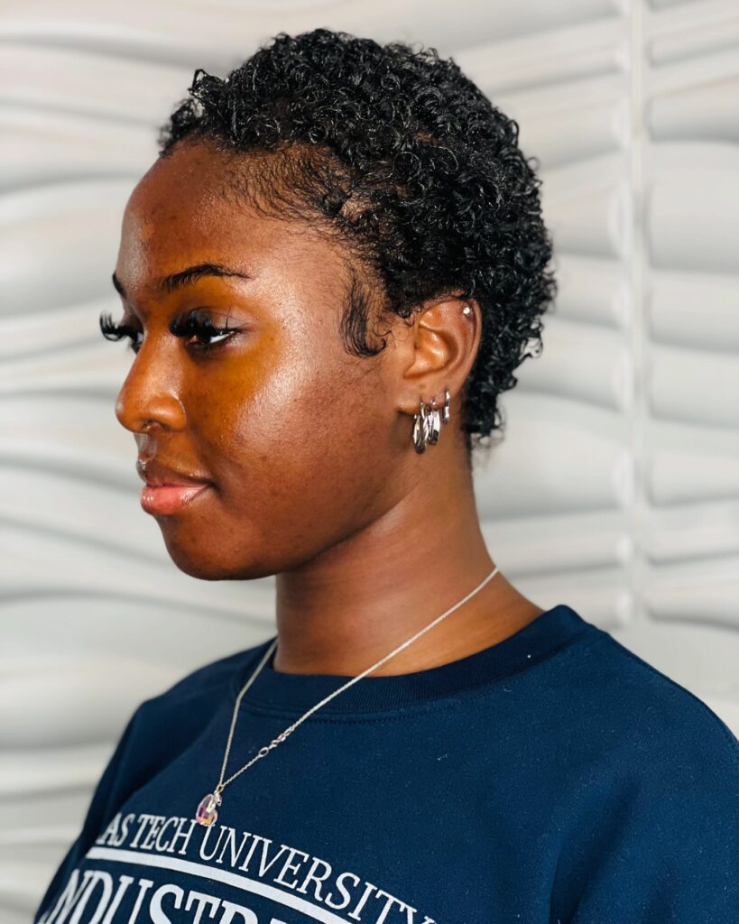 A side profile of a woman with a sleek, jet black, teeny weeny afro and glossy, defined curls.