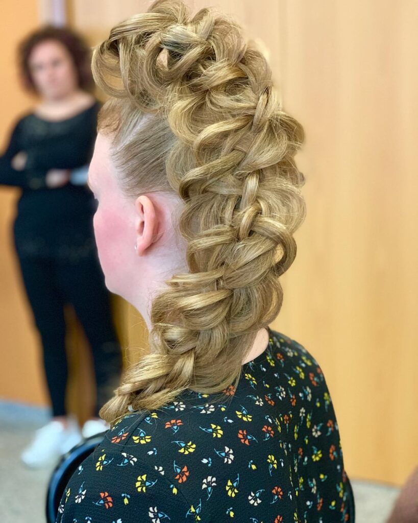 A woman with blonde hair styled into a high-volume braided faux hawk that runs down the center of her head.