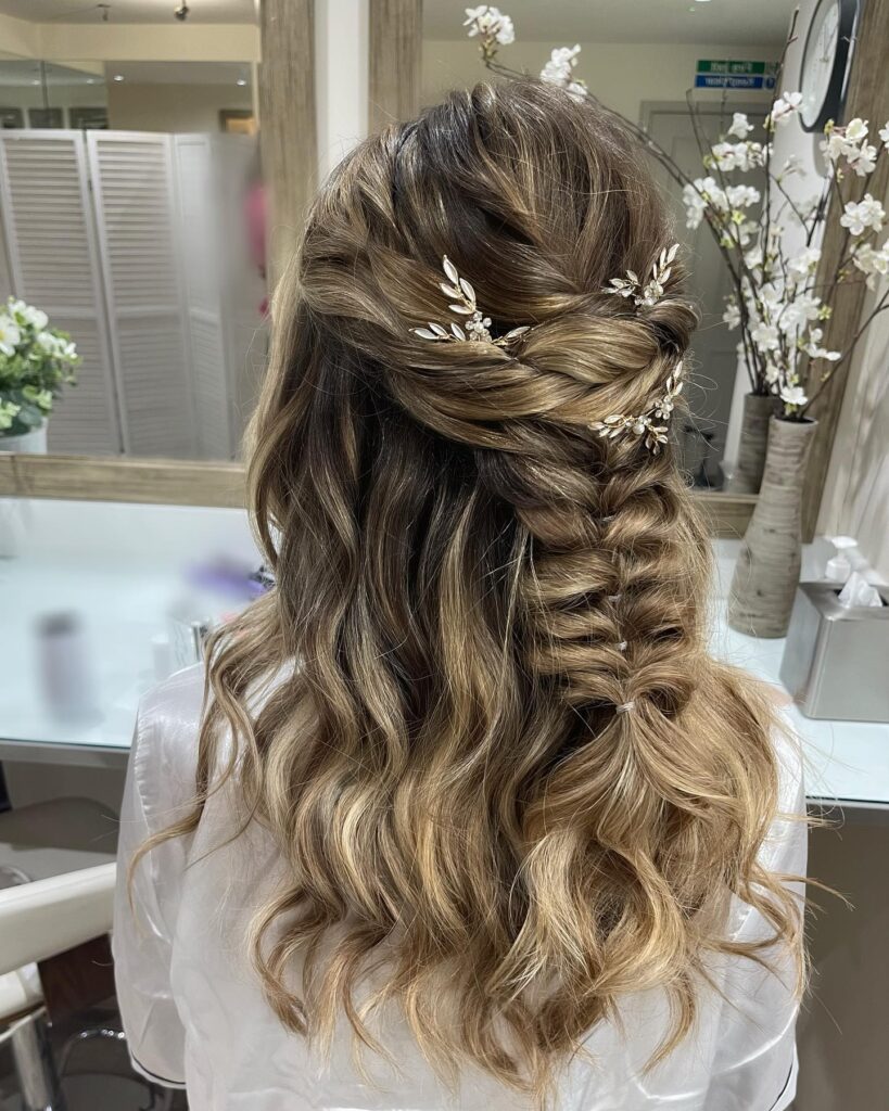 A woman with wavy brunette and caramel hair in a half-up fishtail braid decorated with delicate gold-leaf hair accessories.