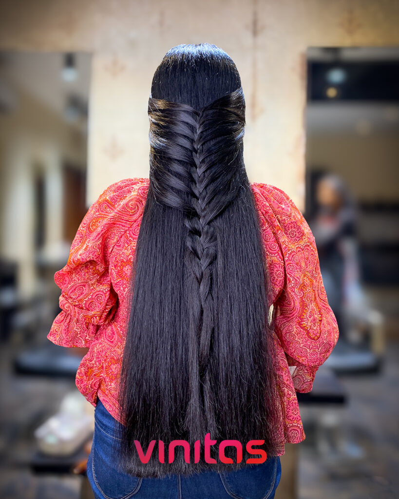 A woman with very long and shiny straight black hair featuring a neat half-up fishtail braid down the center.