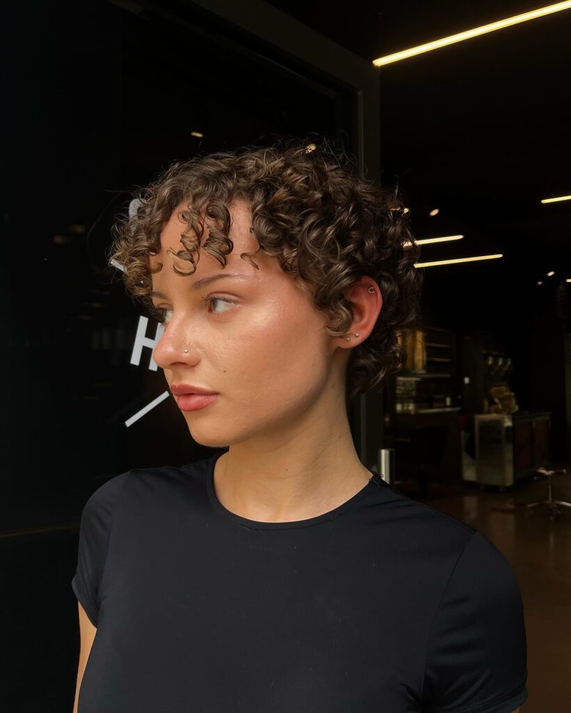 A woman with a light brown curly pixie cut featuring well-defined ringlets that fall softly over her forehead.