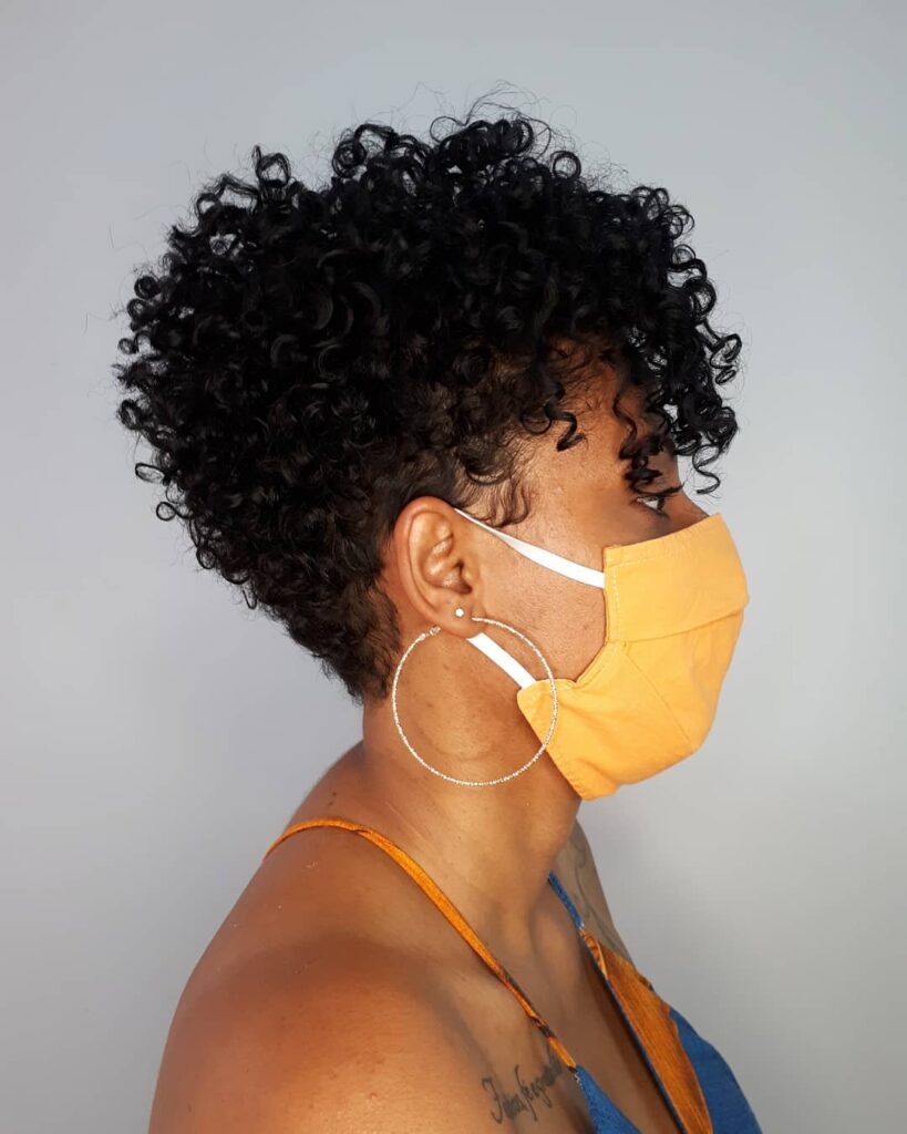 A side view of a woman with a voluminous curly pixie cut featuring tight black coils and tapered sides.