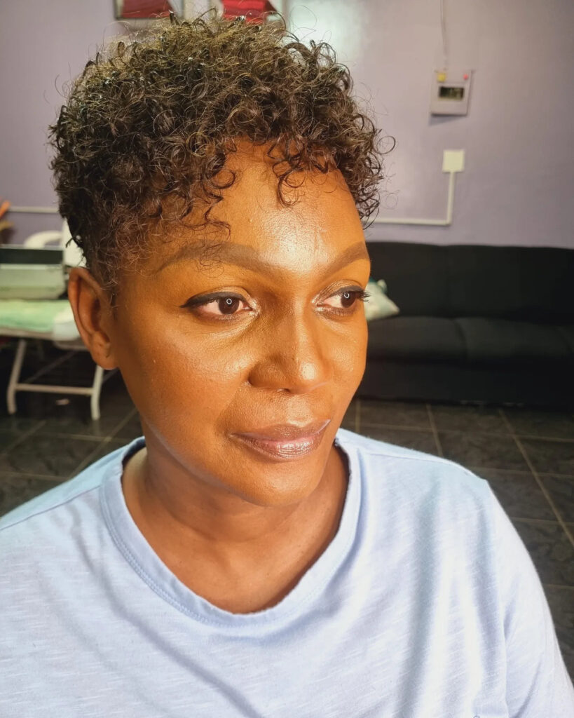 A woman with a short-cropped pixie cut featuring tight, ashy brown curls and a clean silhouette.