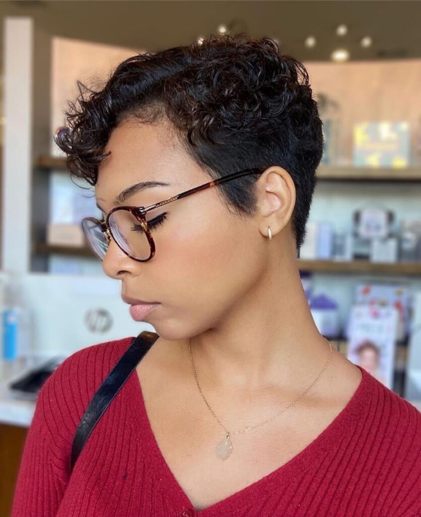 A woman wearing tortoiseshell glasses with a short, dark brown, curly pixie cut that is neatly tapered at the sides and back.