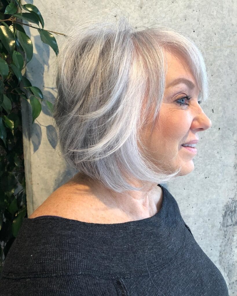 A woman with a textured silver bob featuring wispy face-framing layers and side-swept bangs.