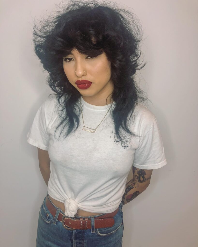 A woman with a voluminous black shaggy hairstyle featuring heavy feathered bangs and long wispy layers.