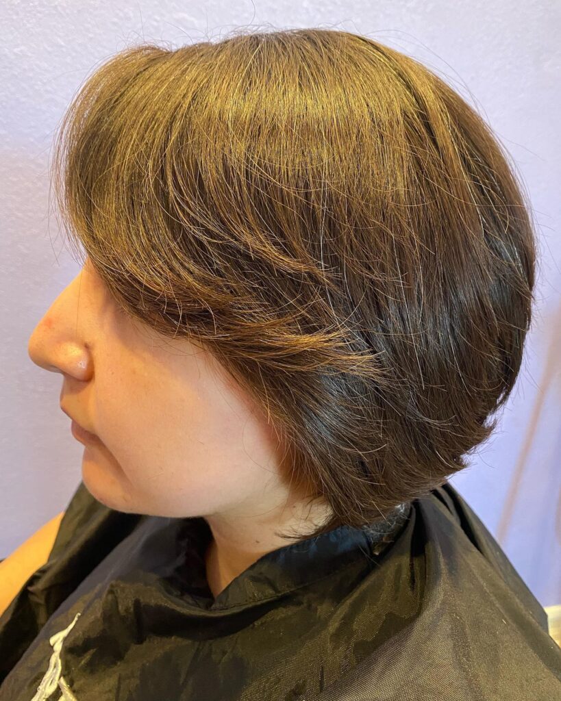 A woman with a short espresso-brown pixie bob featuring soft feathered bangs swept across her forehead.