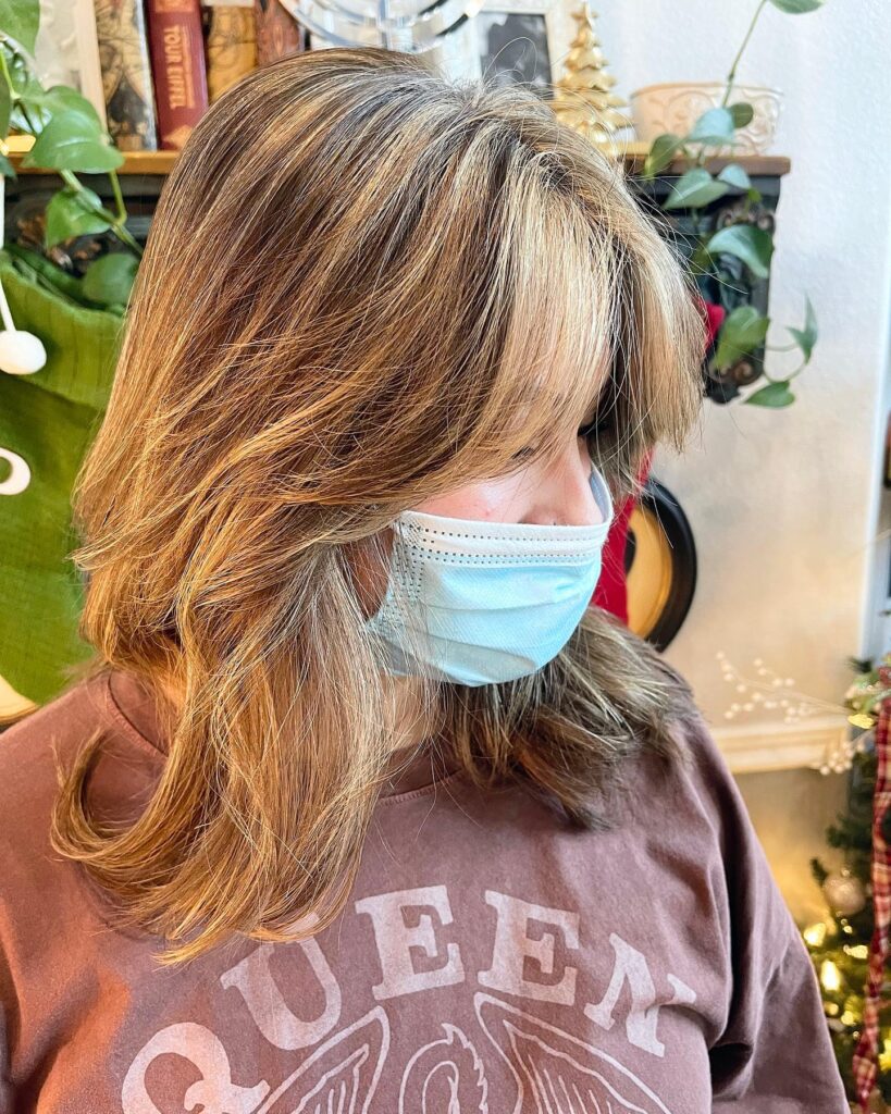 A woman with medium-length caramel-highlighted hair and soft feathered bangs that sweep across her forehead.