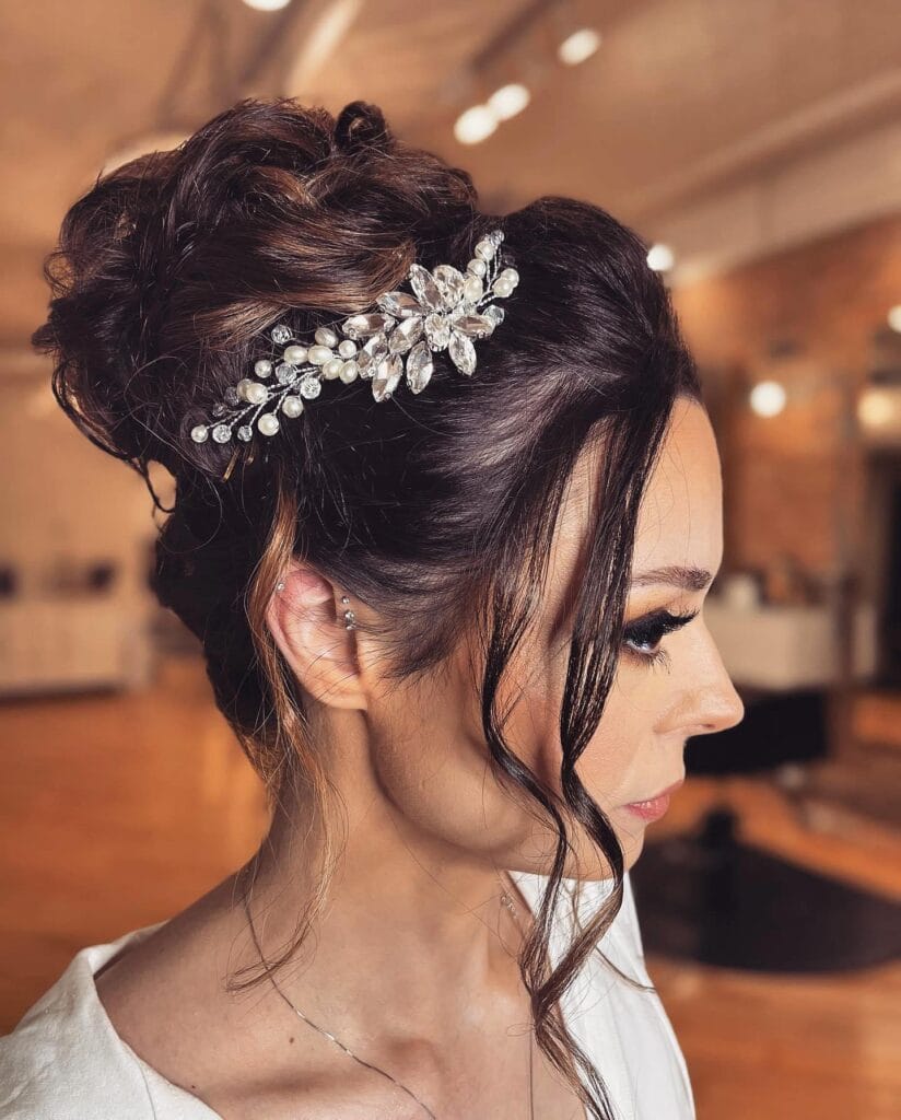 A woman with dark hair styled in a large textured high bun decorated with a shimmering crystal and pearl floral hair vine.