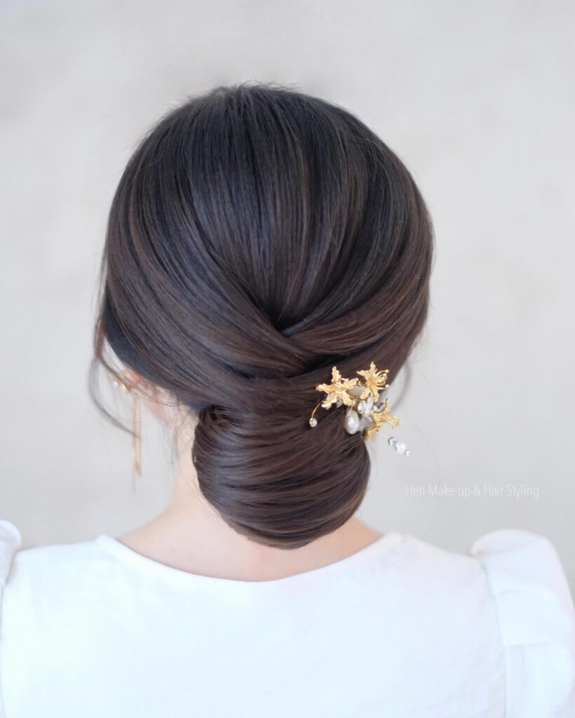 A woman with smooth dark brown hair styled in a criss-cross low chignon featuring a dainty gold star and pearl hair clip.