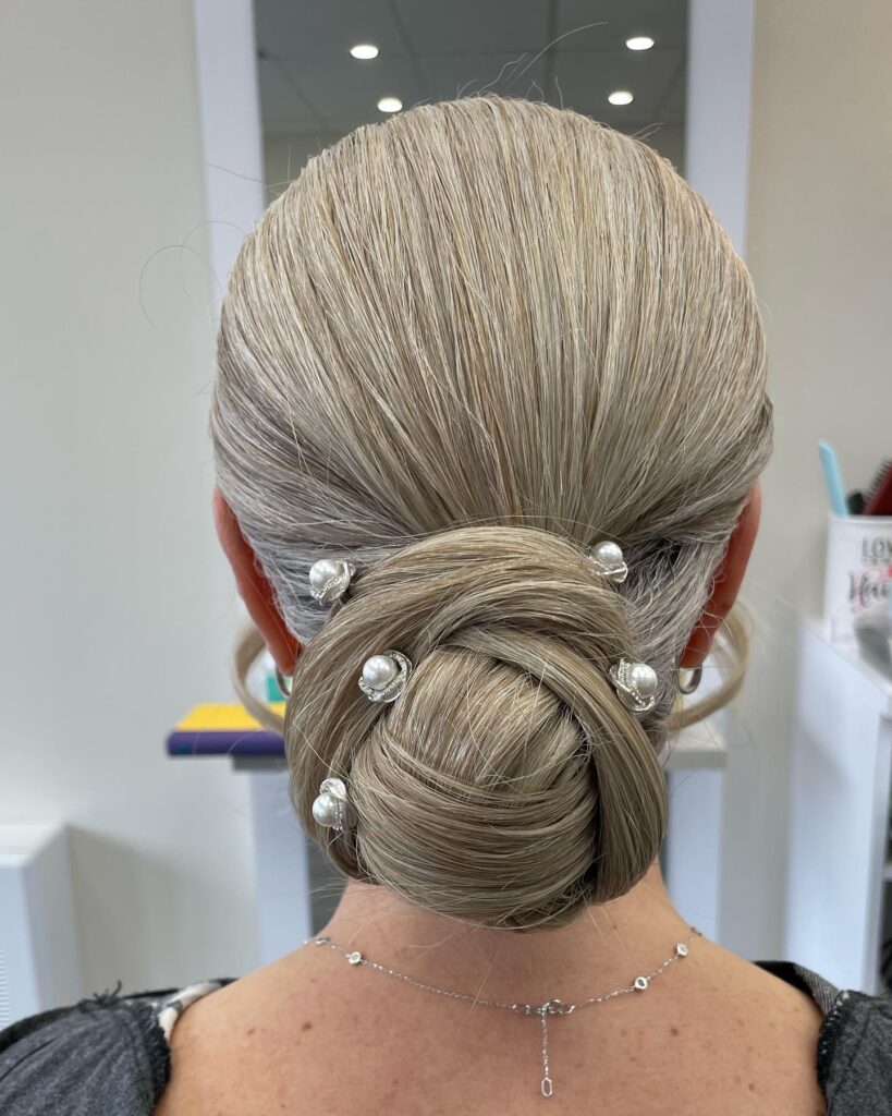 A woman with smooth ash blonde hair styled in a polished low chignon decorated with several scattered pearl and silver pins.