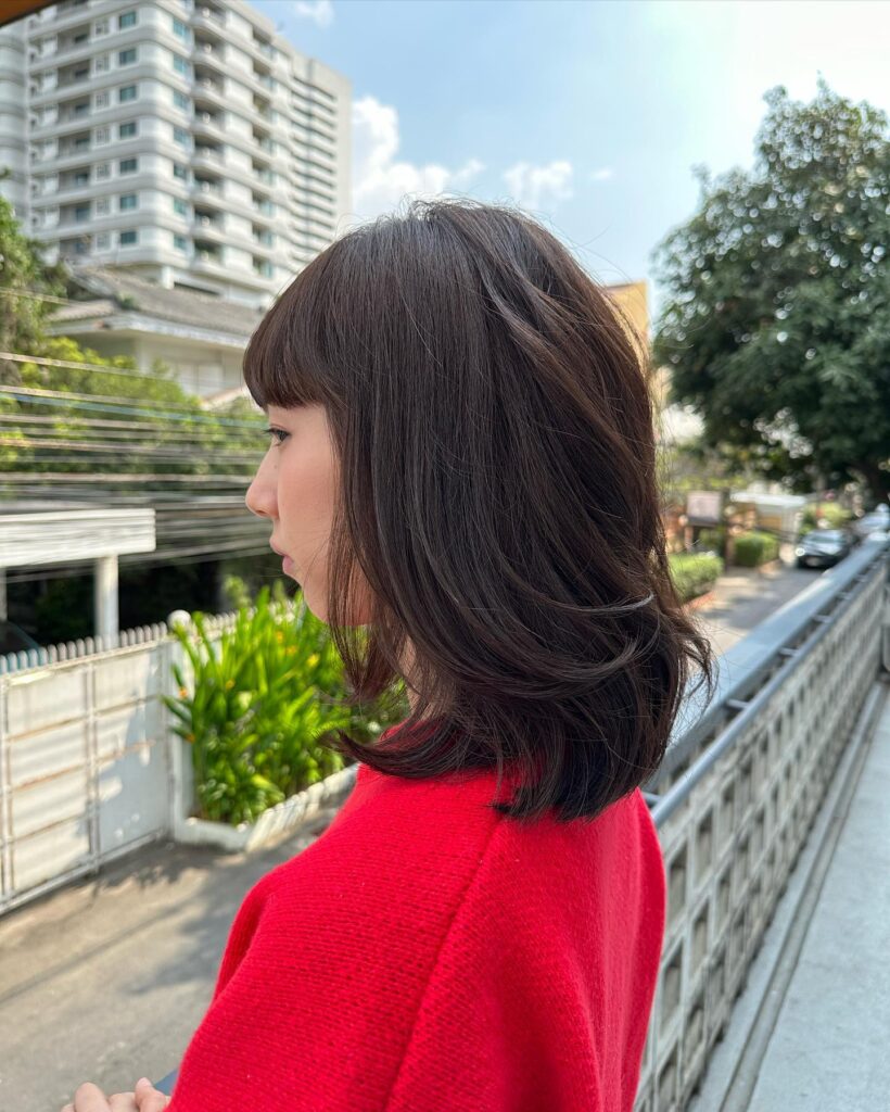 A woman seen from the side with a chocolate brown layered lob and straight-across bangs.