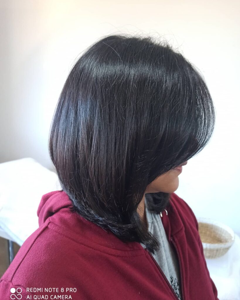 A side profile of a woman with a sleek, jet-black, layered lob styled with a smooth, rounded finish.