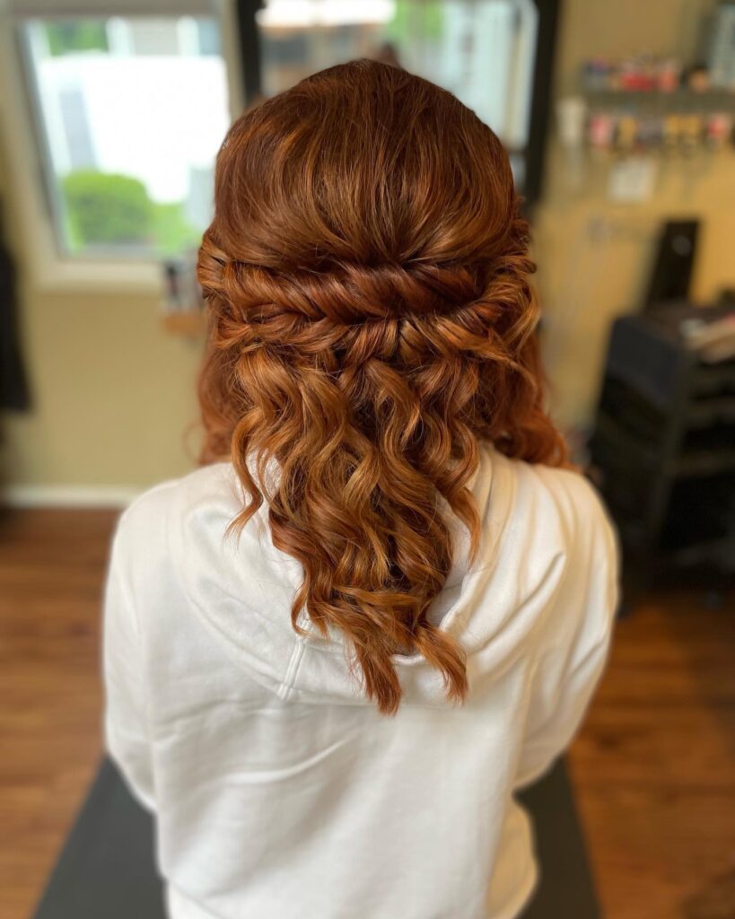 A woman with medium-length, vibrant ginger hair is styled in a horizontal twist with bouncy ringlet curls falling down her back.